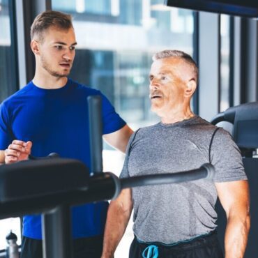 Personal trainer giving instructions to older man at the gym
